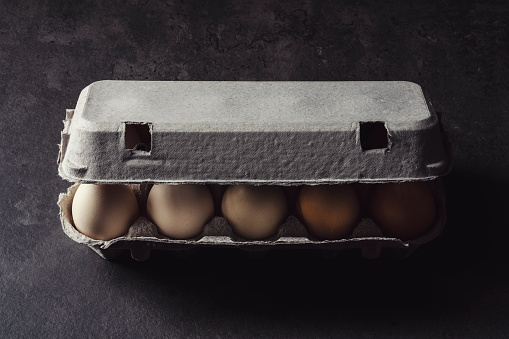 Box of color gradient brown eggs, rectangular egg carton on grey background. Easter eggs. Shot from directly above.