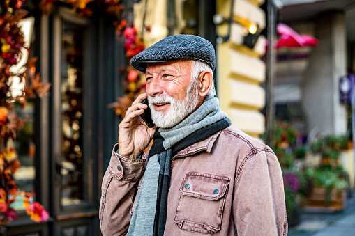 Happy bearded senior man talking by phone. Cheerful senior businessman talking by smartphone. Portrait of modern senior man speaking by phone outdoors