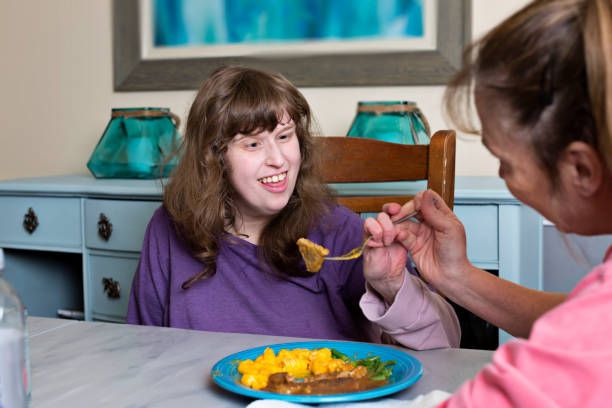 Caretaker assists disabled young adult eating her dinner - fotografia de stock