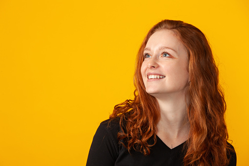 Close up studio portrait of 18 year old woman with long curly red hair on yellow background