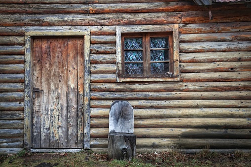 Wall of a cabin made out of wood with a chair and a window outside in the wild
