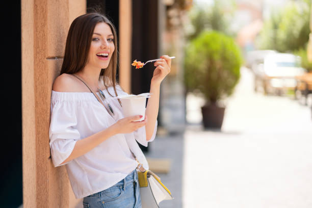 fröhliche frau isst fast food auf der stadtstraße - fine art portrait portrait street looking at camera stock-fotos und bilder