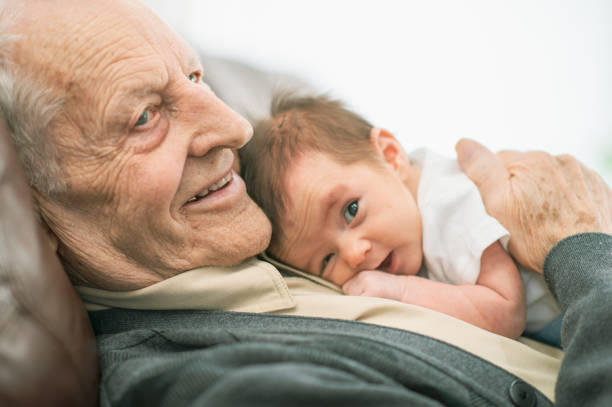 A grandfather of Caucasian ethnicity is spending time with his newborn grandchild. The baby is laying down on his chest.