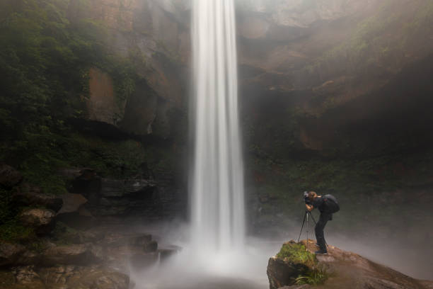 istock Young man standing below a rushing waterfall photographing with tripod in national park wilderness of Australia 1300757774