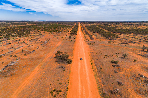 Straight red orange dirt road in outback Australia with single car driving