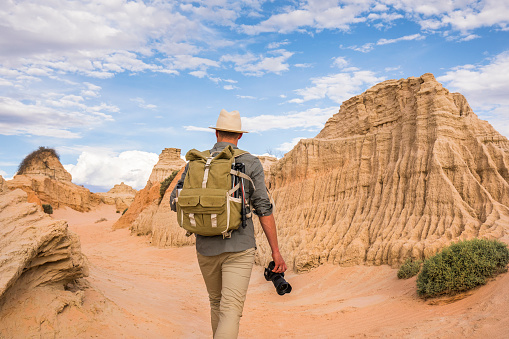 Young man walking in desert with photography backpack on an adventure in outback Australia