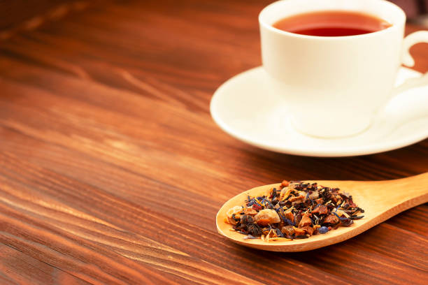 tea mug and tea leaves dried tea leaves in a wooden spoon and brewed tea in a white mug in the background food sample cups stock pictures, royalty-free photos & images