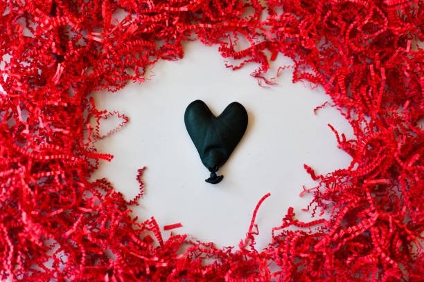istock Chaotic Love - Deflated Black Heart Balloon Surrounded by Red Confetti 1300763111