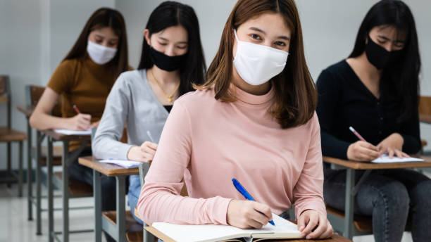 istock Group of college students wearing a face mask and keep distance while studying in the classroom and college or university campus to prevent COVID-19 pandemic. The new college or university campus life 1300766320
