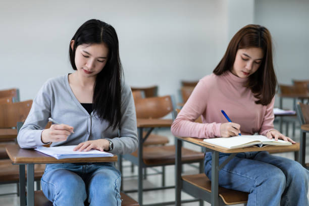 Young woman college students sitting on lecture chair in classroom studying, writing on examination paper answer sheet in doing the final examination test. College students in the classroom present campus life concept. jóvenes estudiantes universitarios sentados en la silla de conferencia en el salón de clases estudiando, escribiendo en la hoja de respuestas de papel del examen al hacer la prueba final del examen. los estudiantes universitarios en el aula presentan el