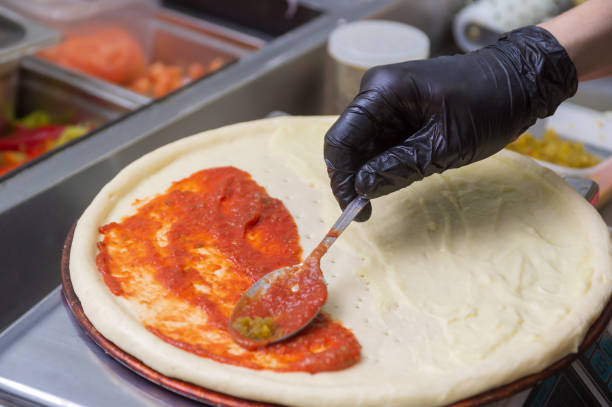 istock Cooking pizza, spreads the first layer of tomato. 1300778060