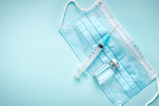 Blank vaccine vial, medical mask and syringe blue background with copy space