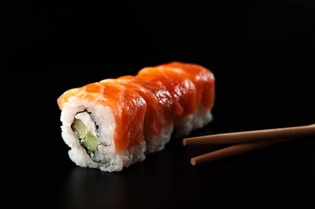 istock Salmon sushi nigiri in chopsticks over black background 1300787647