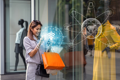 Mujer asiática que utiliza el teléfono móvil inteligente para comprobar el pedido de compra en línea se completa a través de la tecnología omni canal con ropa junto a las gafas en la tienda con acción feliz en el centro del departamento photo