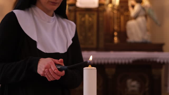 Nun in a Catholic church lights up a candle.
