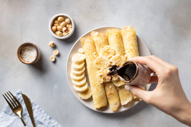 female hand pours date syrup over rolled banana pancakes female hand pours date syrup over rolled banana pancakes. Healthy vegan food concept. blurred background. top view. date syrup stock pictures, royalty-free photos & images