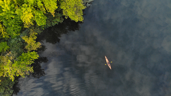 Top aerial view of the river along which a small orange kayak floats. Green trees grow on the shore. Ecosystem. Ukraine