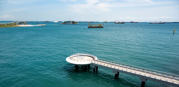 A pier in the harbour of Singapore seen a warm summer day. In the back big cargo ships.