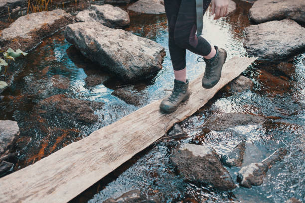 wandermädchen watet auf einem holzbrett über den fluss, schwere wanderstiefel - mountain pass stock-fotos und bilder