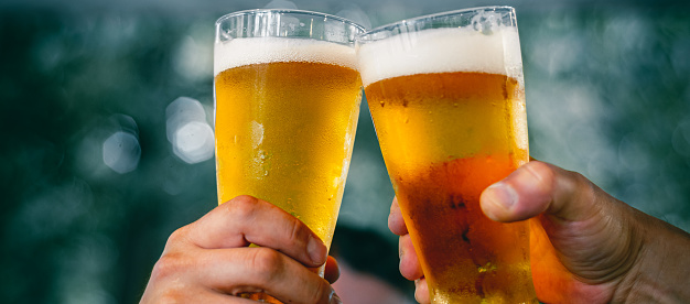 Close-up view of a two glass of beer in hand. Beer glasses clinking at outdoor bar or pub