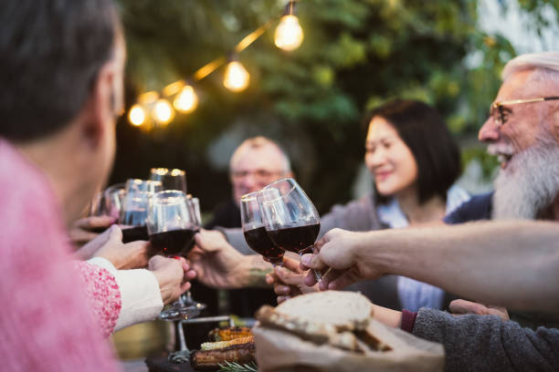 happy family dining and tasting red wine glasses in barbecue dinner party - ludzie w różnym wieku i pochodzeniu etnicznym bawią się razem - dining senior adult friendship mature adult zdjęcia i obrazy z banku zdjęć