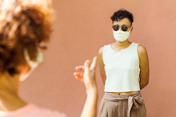 istock Two women wearing protective mask talking, keeping social distance 1300807177