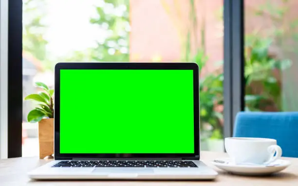 Mockup of laptop computer with empty screen with coffee cup on table of the coffee shop background,green screen