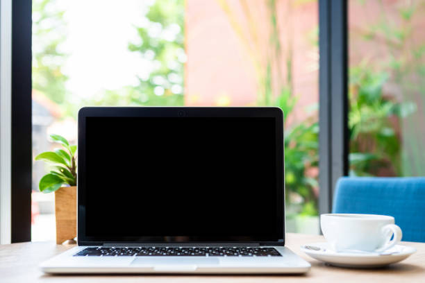 istock Mockup of laptop computer with empty screen with coffee cup on table of the coffee shop background,Black screen 1300807729