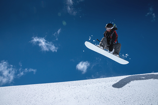Woman athlete snowboarder in flight after jumping on a snowy slope against a background of a dark blue sky.