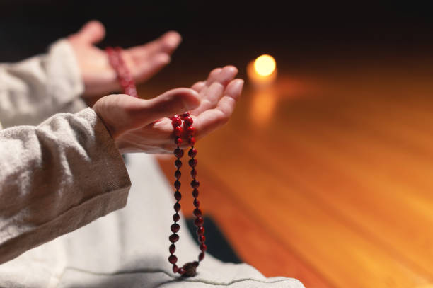 close-up of a male practitioner's hand sitting in lotus position in a dark meditation room with a rosary in his hands - om mantra imagens e fotografias de stock
