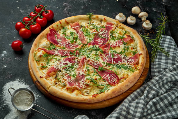 istock Appetizing italian pizza with cheese, prosciutto, arugula and parmesan in a composition with ingredients on a black background 1300810124