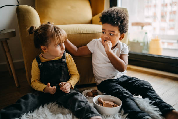 It's delicious Kids sitting in living room and eating snacks from bowl boys bowl haircut stock pictures, royalty-free photos & images