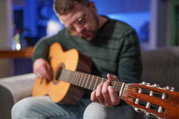 istock Young man sitting at home on sofa and playing guitar 1300815219