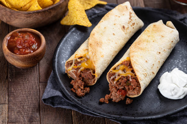 Beef Burritos With Beans and Cheese Burritos with ground beef, refried beans and cheese on a black plate with salsa and tortilla chips burrito stock pictures, royalty-free photos & images