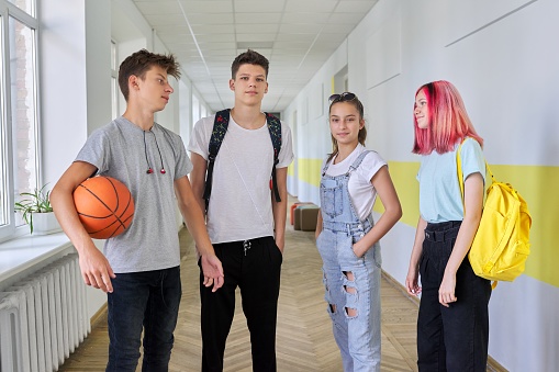 A group of teenage students 16 years old in the school hallway. Walking talking teenagers with backpacks, basketball ball
