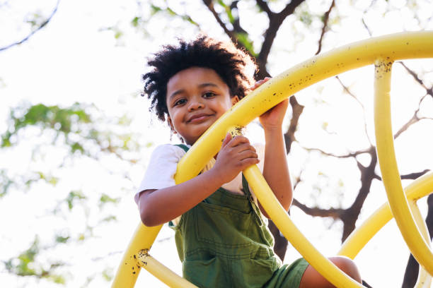 lindo niño afroamericano divirtiéndose mientras jugaba en el patio de recreo durante el día en verano. actividad al aire libre. jugar hace creer el concepto. educación externa - 4 5 años fotografías e imágenes de stock