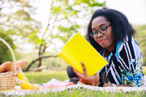 Happy young African American woman reading an interesting book. A cheerful African American woman in the park in the summertime. Young African American student