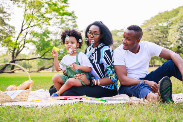 feliz concepto de vida familiar afroamericana. padres afroamericanos (padre, madre) y niño disfrutando durante el juego de burbujas de jabón juntos. familia se relaja en el parque verde. fin de semana familiar. - bubble child bubble wand blowing fotografías e imágenes de stock