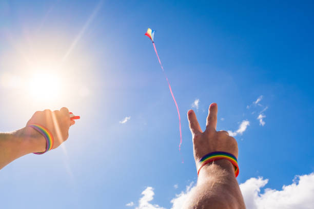 팔과 손의 초상화는 lgtb 색상의 팔찌를 착용하고 하늘에 연을 비행 - pride month 뉴스 사진 이미지