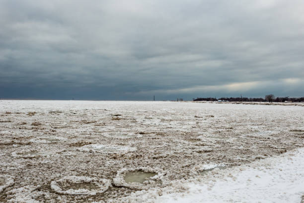 blocos de gelo congelado e areia criando formas circulares flutuando em cima de um lago muito frio michigan em dia sombrio nublado em chicago - bizarre landscape sand blowing - fotografias e filmes do acervo