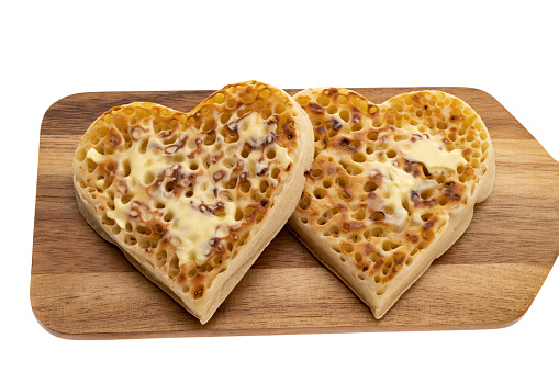 Heart shaped buttered crumpets on a wooden platter - white background