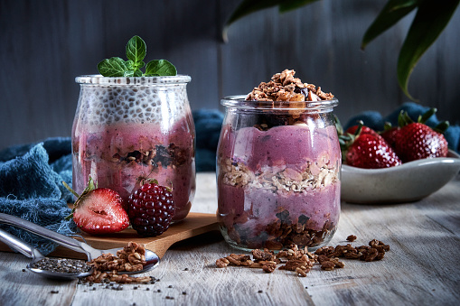 Healthy food: Set of two banana blackberry and strawberry yogurt smoothies with chia and cereal in small bottles on a rustic table.