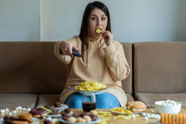 mujer con sobrepeso sentarse en el sofá con comida chatarra - comer demasiado fotografías e imágenes de stock