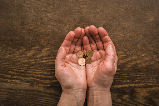 Opened old woman palms with euro coins on dark brown wooden table background. Poverty concept. Point of view shot. Closeup. Top down view.