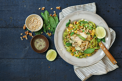 Leftover turkey green pasta with basil-mint pesto, sweet corn, green peas, seeds and microgreen. Flat lay top-down composition on dark wooden background.