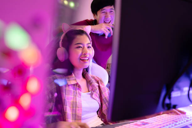 młoda atrakcyjna azjatka grająca w gry wideo w swoim studio z chłopakiem z tyłu. widok z boku pary pracującej przed tą samą stacją roboczą w profesjonalnym studiu projektowym - video game friendship teenager togetherness zdjęcia i obrazy z banku zdjęć
