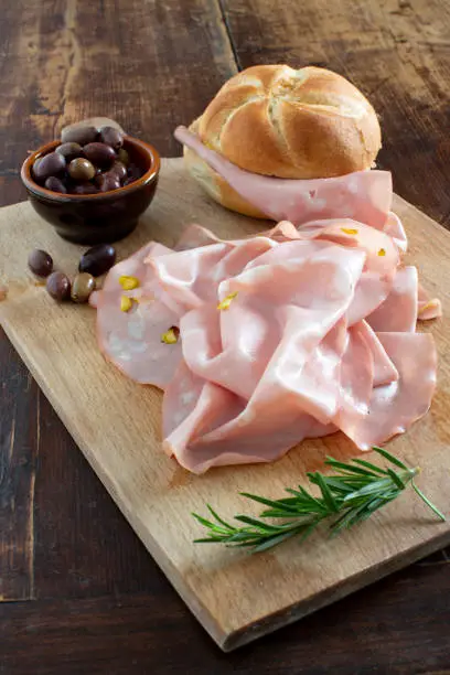 italian mortadella with bun, olives and rosemary on wooden cutting board