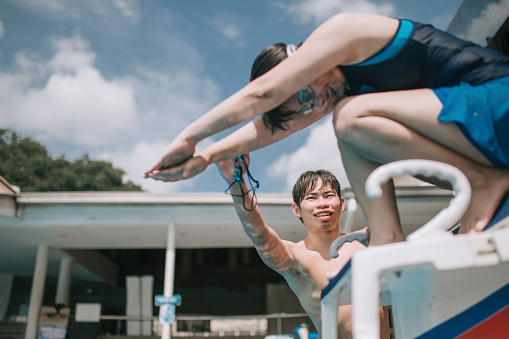 asian chinese swimming coach guiding his adult student diving skill encouraging preparing her diving into water on track starting block