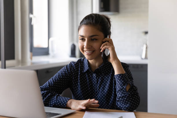 istock Smiling Indian woman work on laptop talking on cellphone 1300836722