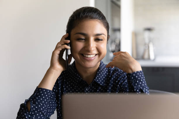 istock Happy Indian woman talk on smartphone working on laptop 1300836727